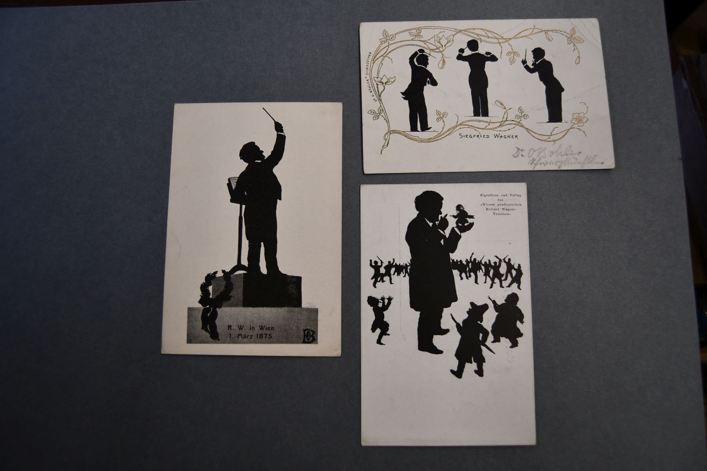 3 Bildpostkarten. Silhouetten von Richard Wagner (2) und Sohn Siegfried (1). U.a. Richard Wagner als Dirigent (Wien, 1. März 1875) und umgeben von zwerghaften Kritikern, von denen er einen (wohl Eduard Hanslick) auf der Hand trägt. Beiliegt eine Silhouette von Richard Wagner als Dirigent (Musikverein WIen, 14.3.1875) aus dem "Merker", Heft 9, 1910.